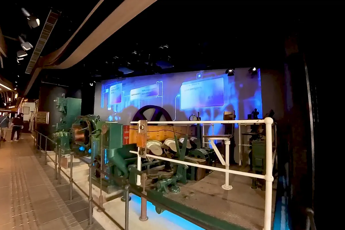 Old winding machinery from the Peak Tram on display in a dark hall at the Central Terminus, with a lit screen behind it